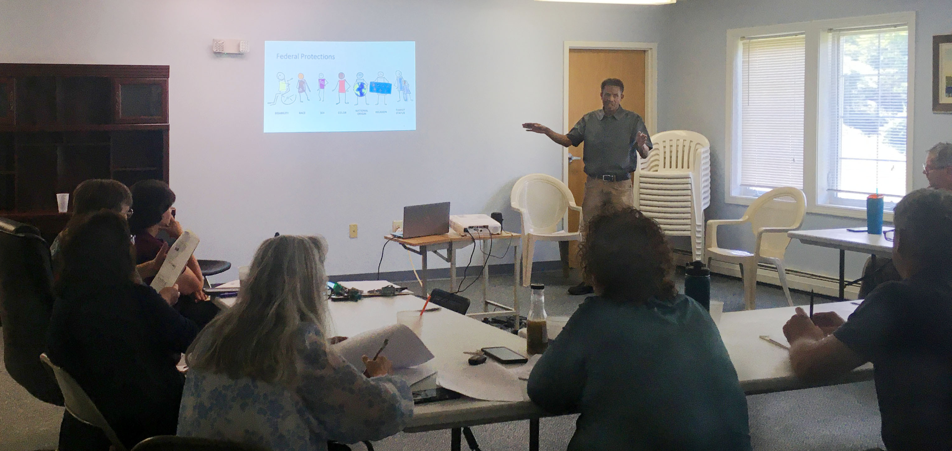 Person presenting a Fair Housing workshop to a group of people seated at tables